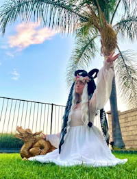 a woman in a white dress sitting on the grass with a palm tree in the background
